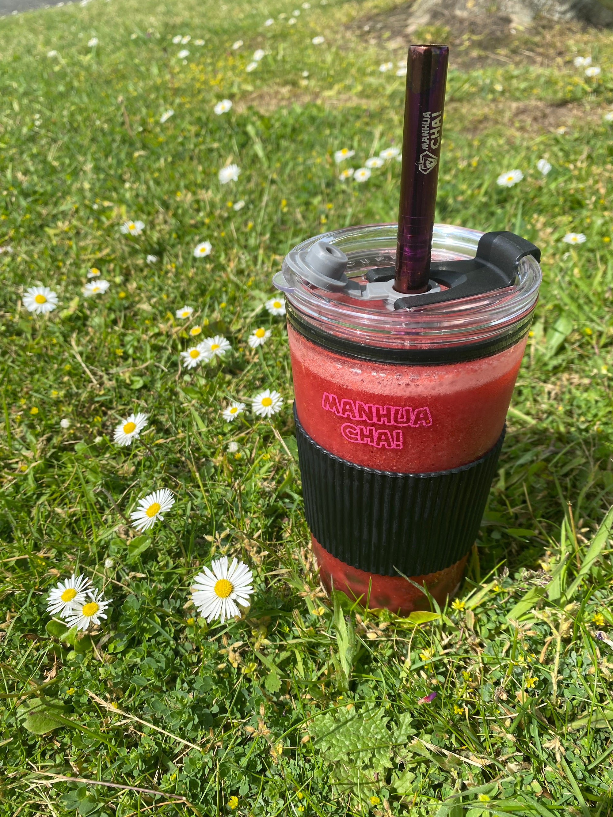 bubble tea cup filled with red strawberry slush sitting on the grass surrounded by daisies